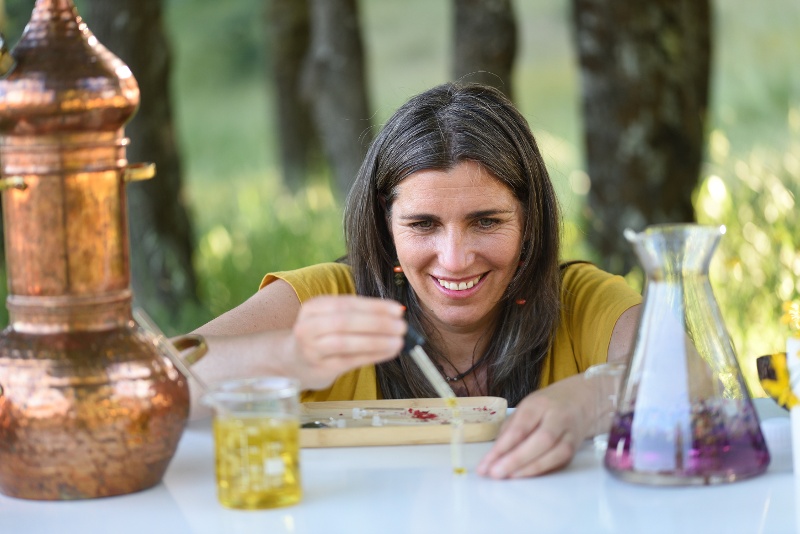 A woman crafting with natural dyes at a table outdoors, smiling as she works.